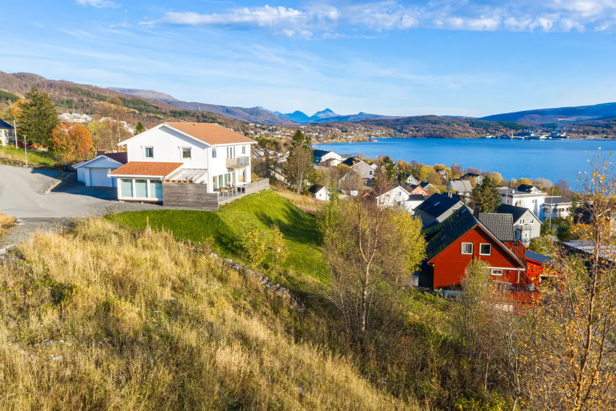 Utsikt mot øst fra tomta, med nabohus og sjøen.